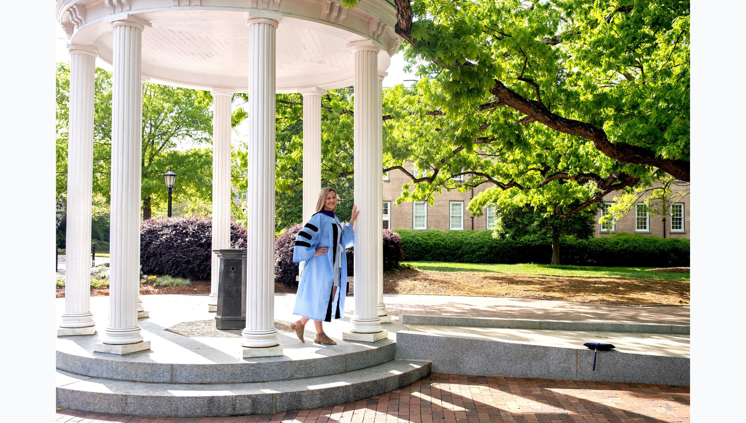 A student posing for a graduation photo at the Old Well.